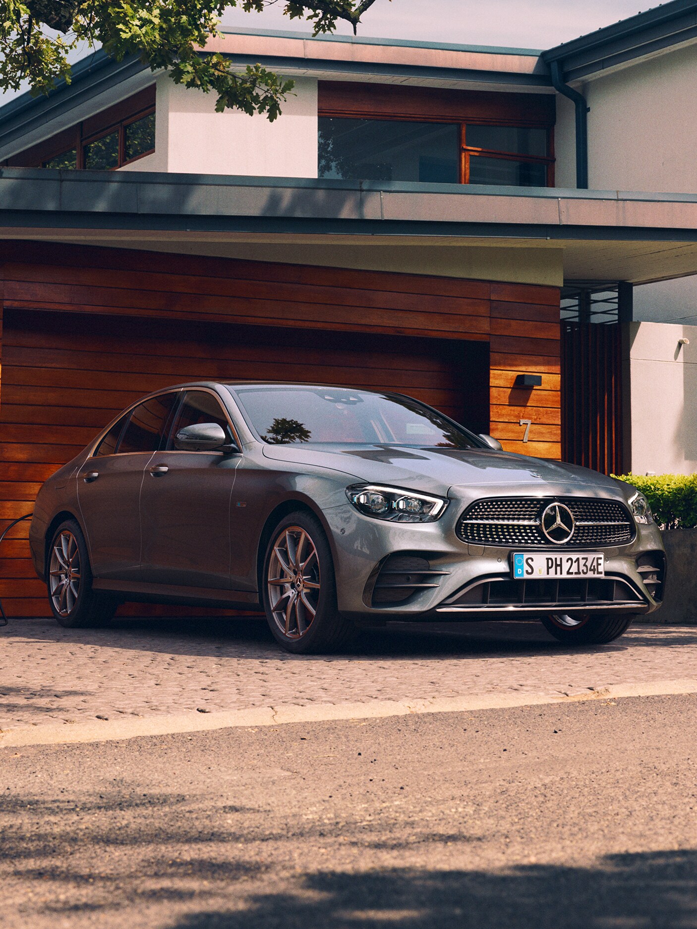 The image shows the Mercedes-Benz E-Class Saloon being charged outside a garage.