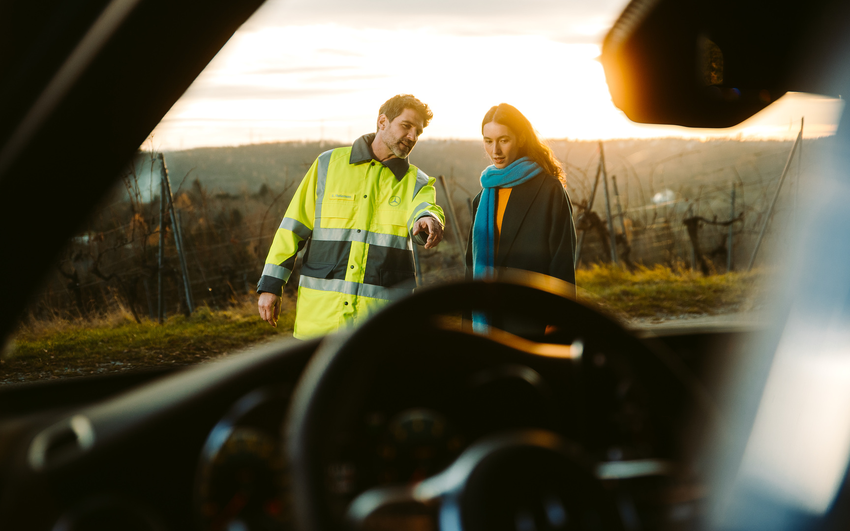 Breakdown and damage assistance | Mercedes-Benz Through the windscreen of a Mercedes we see a service technician standing next to the driver in front of the vehicle and pointing at it to explain something.
