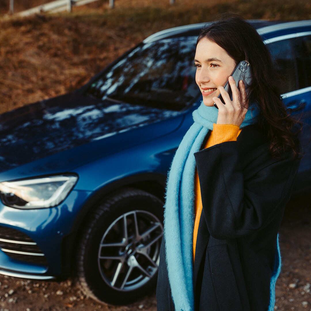 A woman standing in front of her Mercedes SUV, talking on a smartphone.