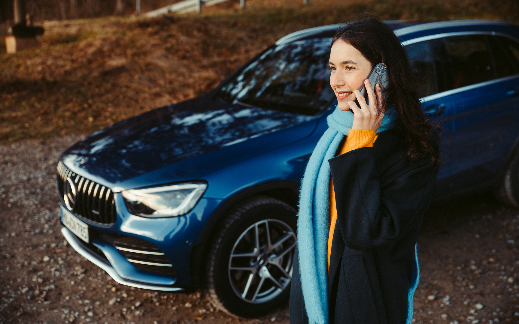 บริการช่วยเหลือเมื่อรถเสีย | Mercedes-Benz ผู้หญิงคนหนึ่งยืนพิงรถยนต์ Mercedes-Benz และจ้องสมาร์ทโฟนของเธอ
