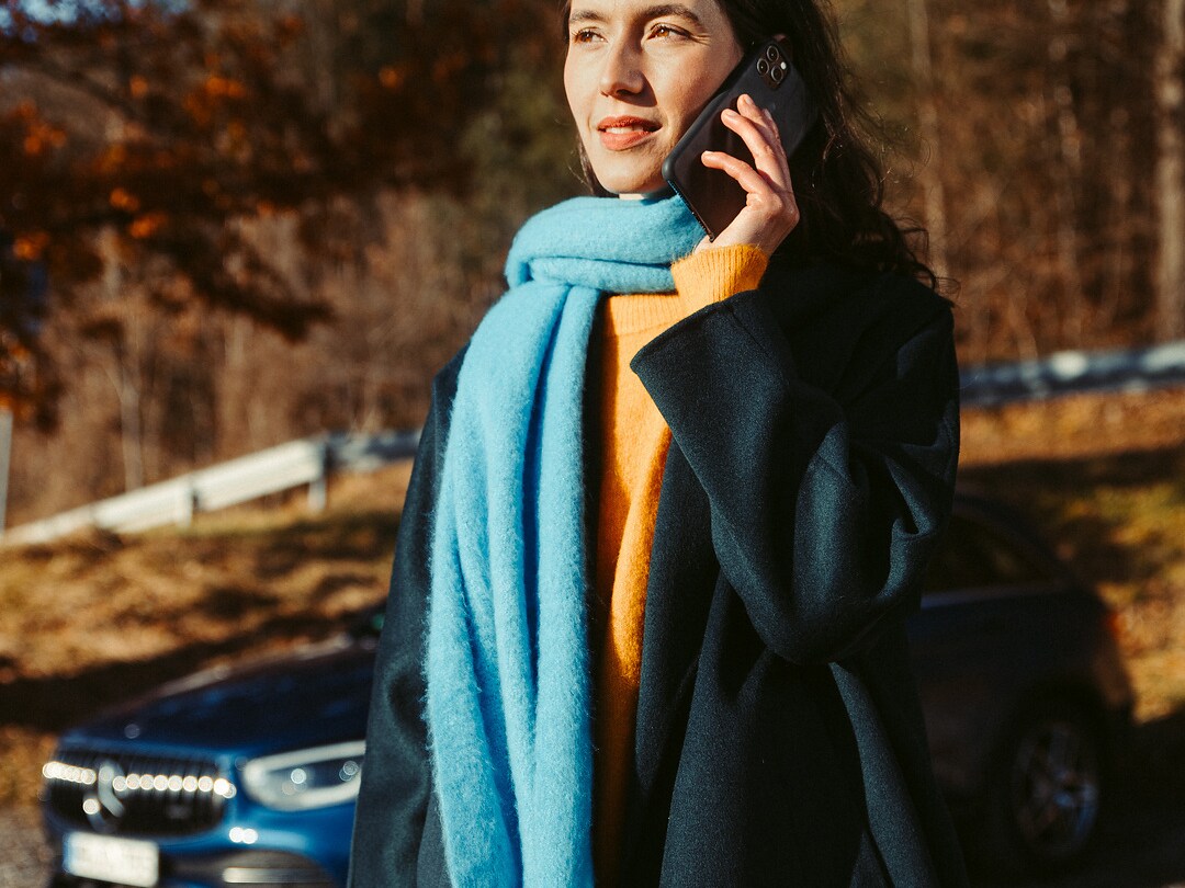 A woman standing in front of her Mercedes SUV, talking on a smartphone.