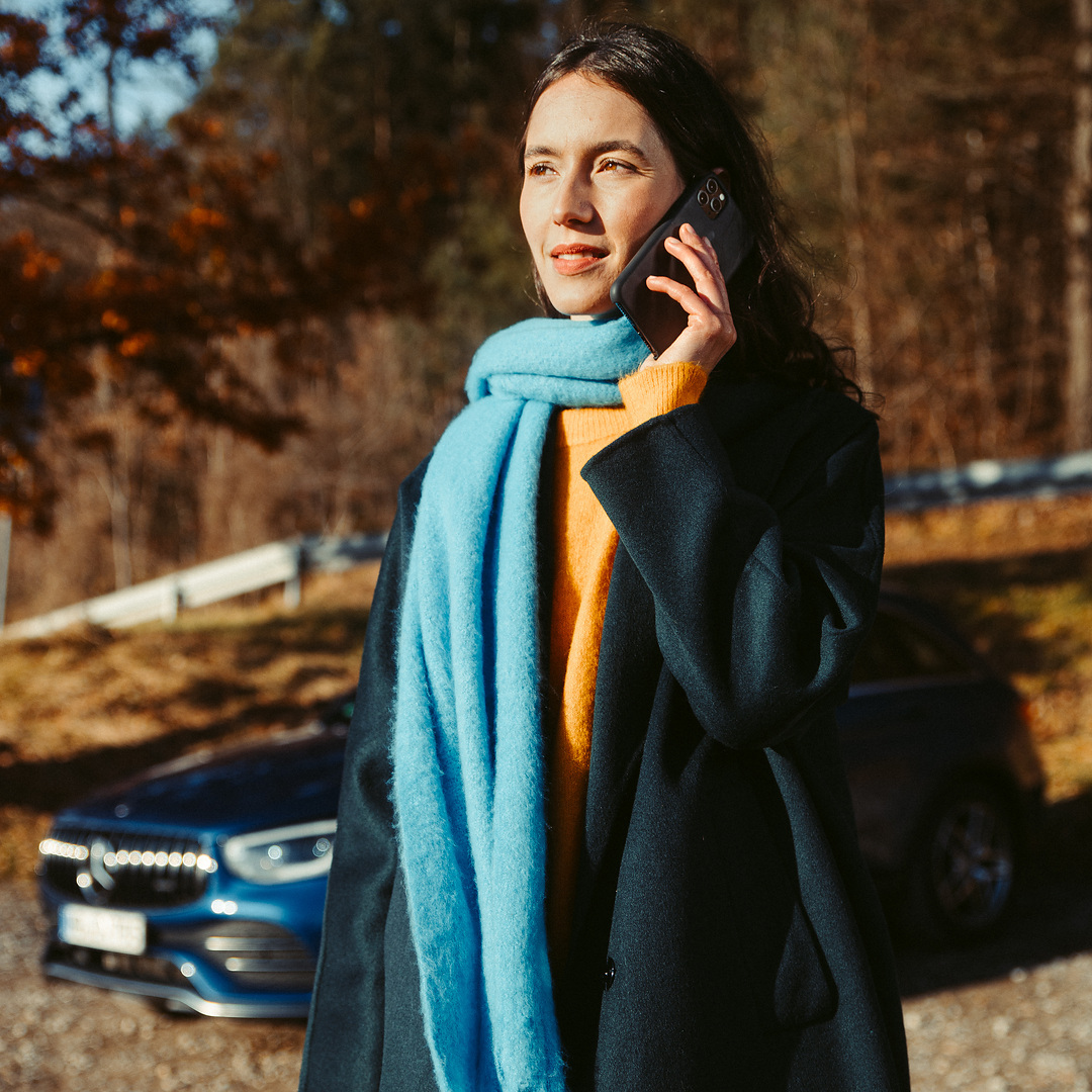 When the ride ends unexpectedly | Breakdown Assistance Overview | Mercedes-Benz A woman standing in front of her Mercedes SUV, talking on a smartphone.