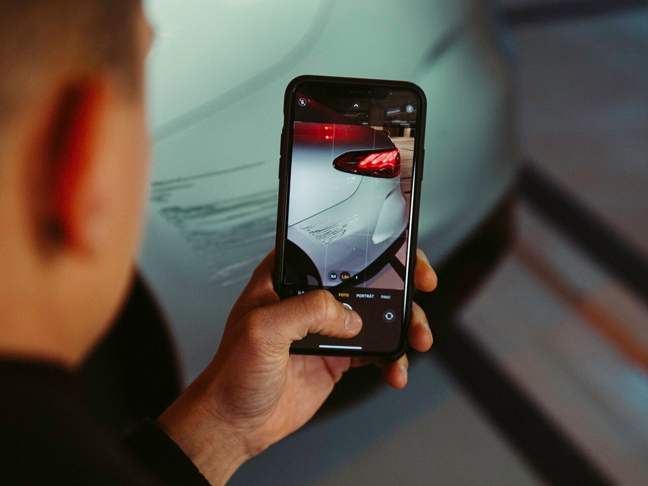 Using a smartphone, a man is photographing the damage to the rear wing of his Mercedes.