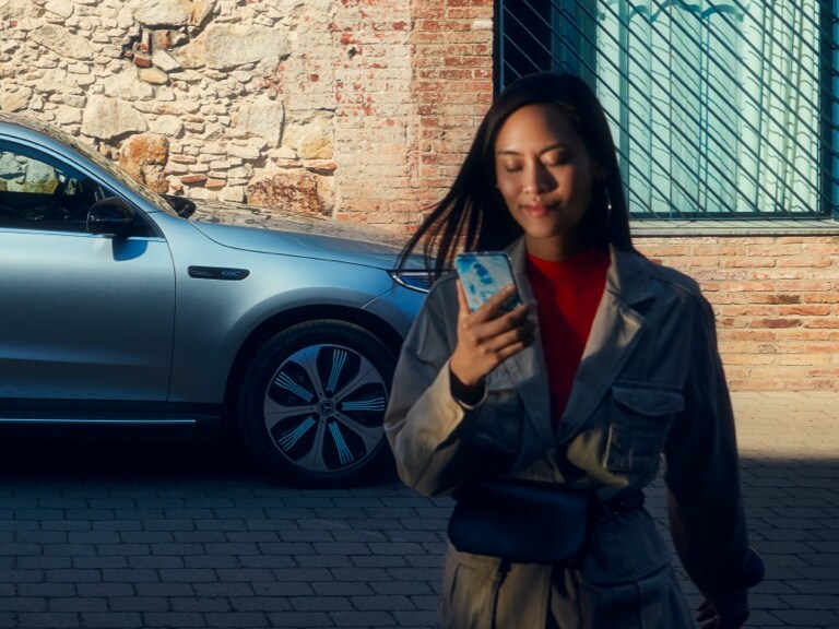 A woman uses the Mercedes me App on her smartphone to connect to her Mercedes-Benz.