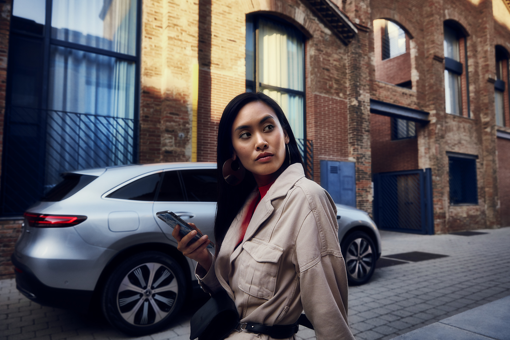 Online appointment booking | Mercedes-Benz A lady standing in front of her Mercedes with a smartphone in her right hand.