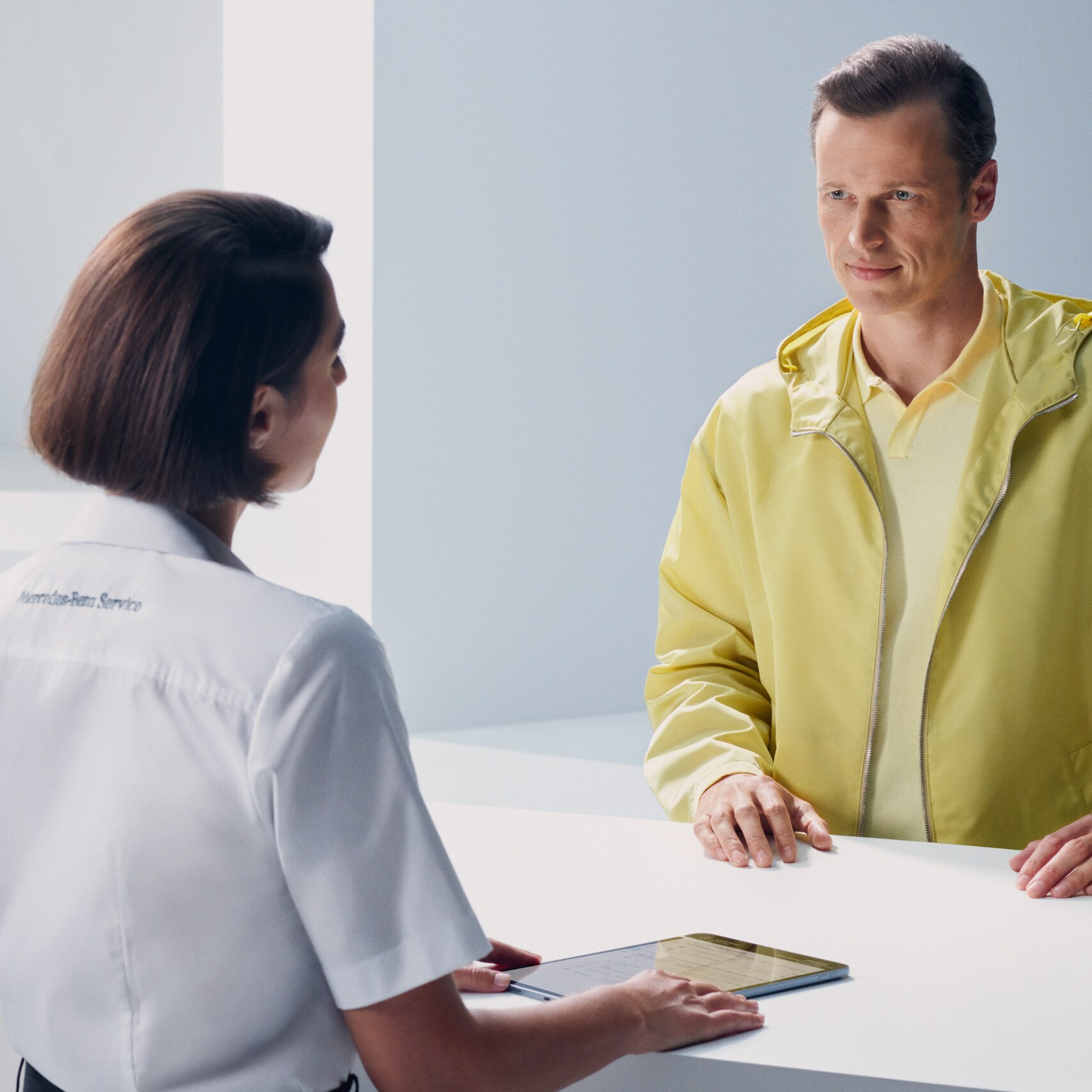 ลูกค้ายืนพิงเคาน์เตอร์และหันไปหาพนักงานของ Mercedes-Benz ด้วยความคาดหวัง