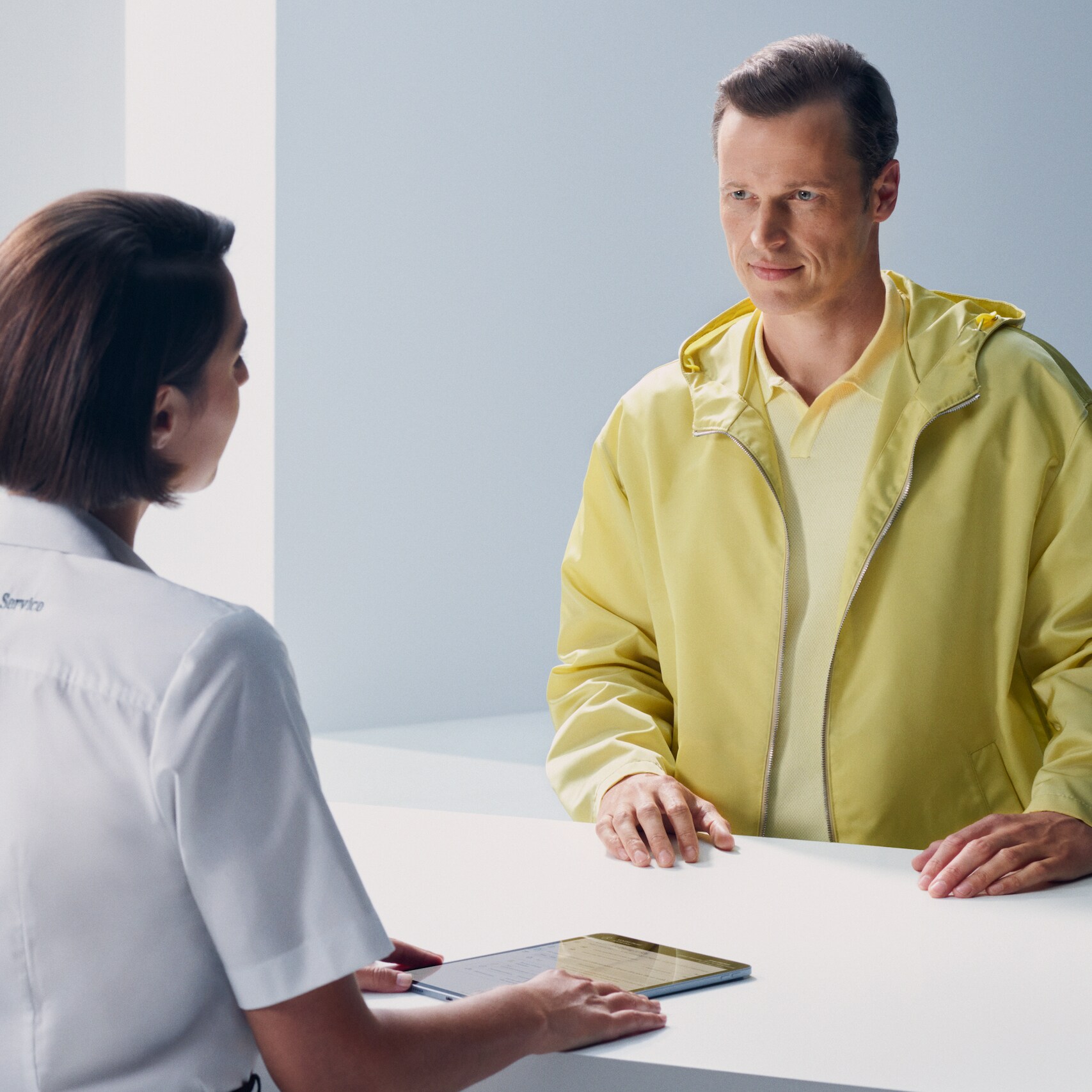 A customer leaning at the counter turns expectantly to face a Mercedes-Benz employee.