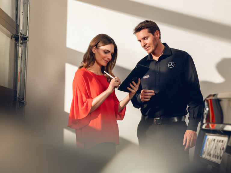 Seemingly genuine: look out for counterfeit parts | Genuine Parts | Mercedes-Benz A woman signs a document on a tablet in the workshop.