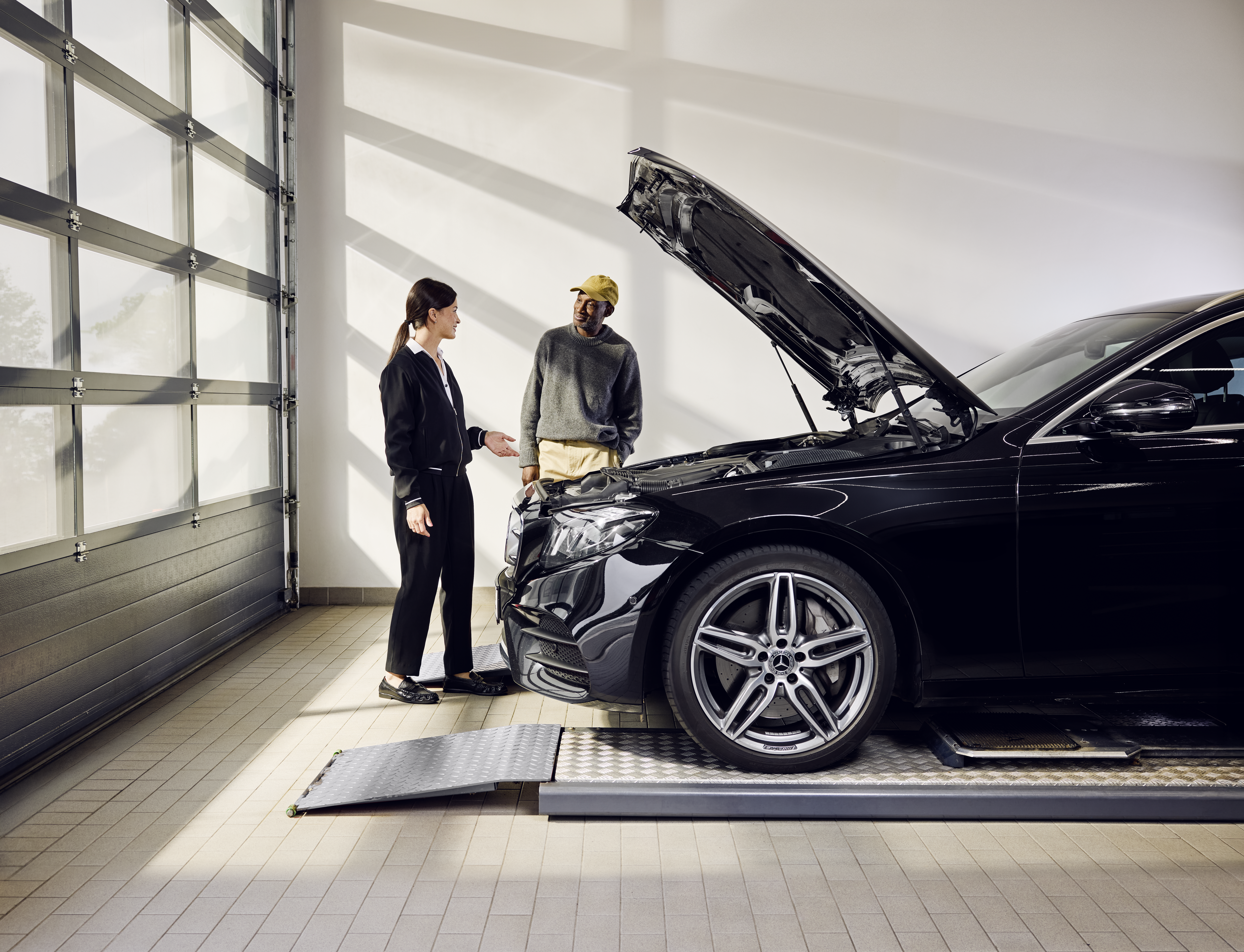 การเปลี่ยนอะไหล่แท้ Mercedes-Benz รถยนต์ Mercedes‑Benz จอดอยู่บนพื้นยกระดับสำหรับซ่อมบำรุงโดยเปิดฝากระโปรงหน้าทิ้งไว้ ระหว่างขั้นตอนการเปลี่ยนอะไหล่แท้โดยช่างผู้ชำนาญการที่ศูนย์บริการ.