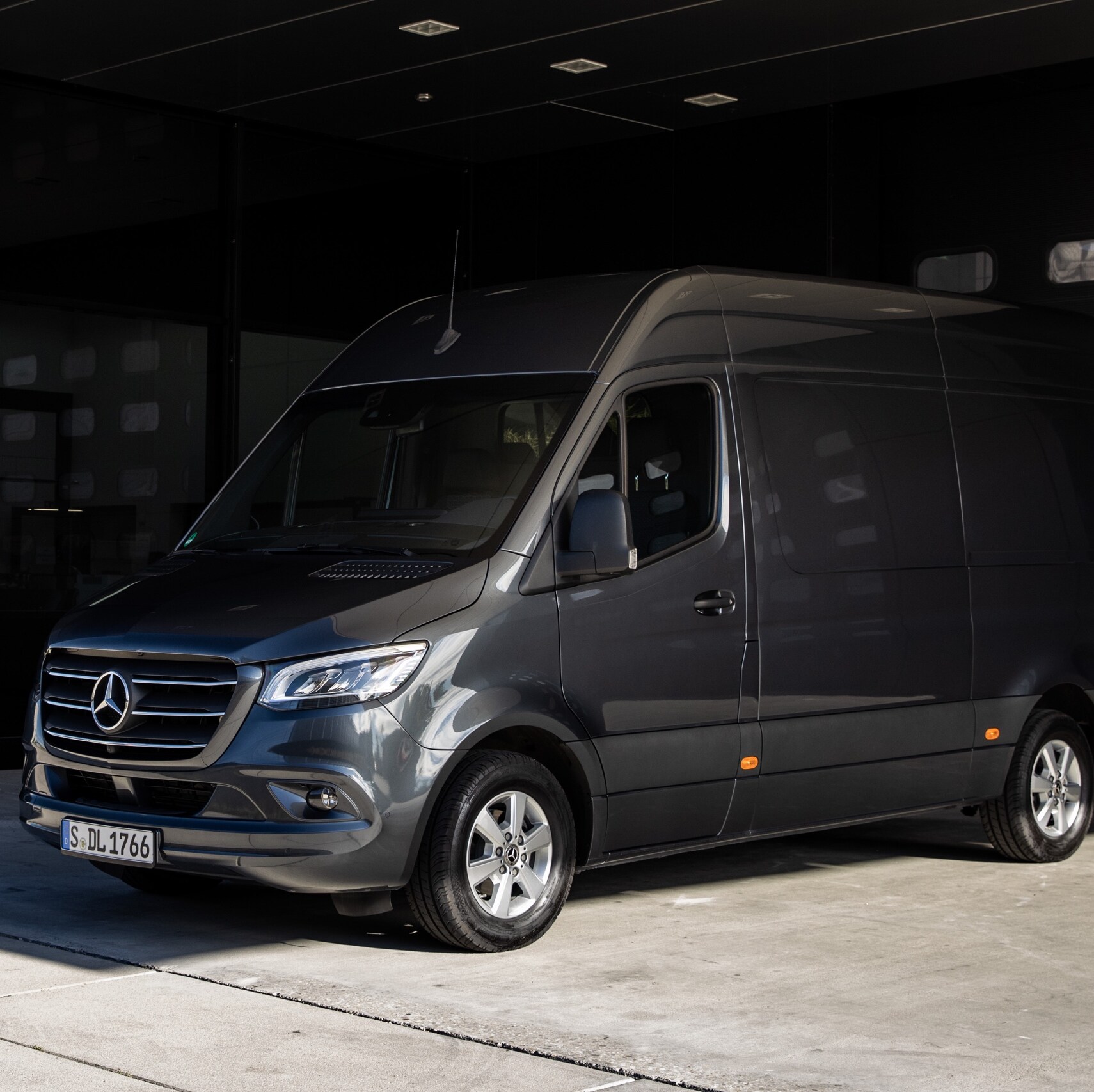 A Sprinter panel van from Mercedes-Benz standing in front of a sliding gate in a modern courtyard.
