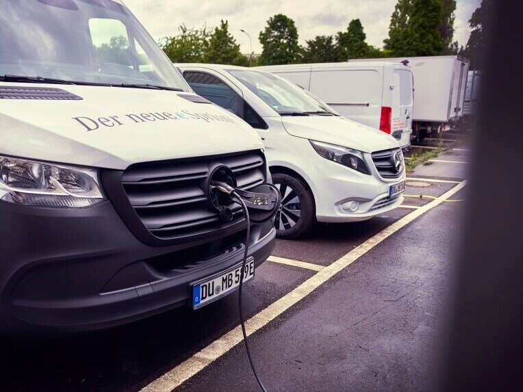 The eSprinter, an electric van from Mercedes-Benz, charging at a charging station. In the background further electric vans can be seen.