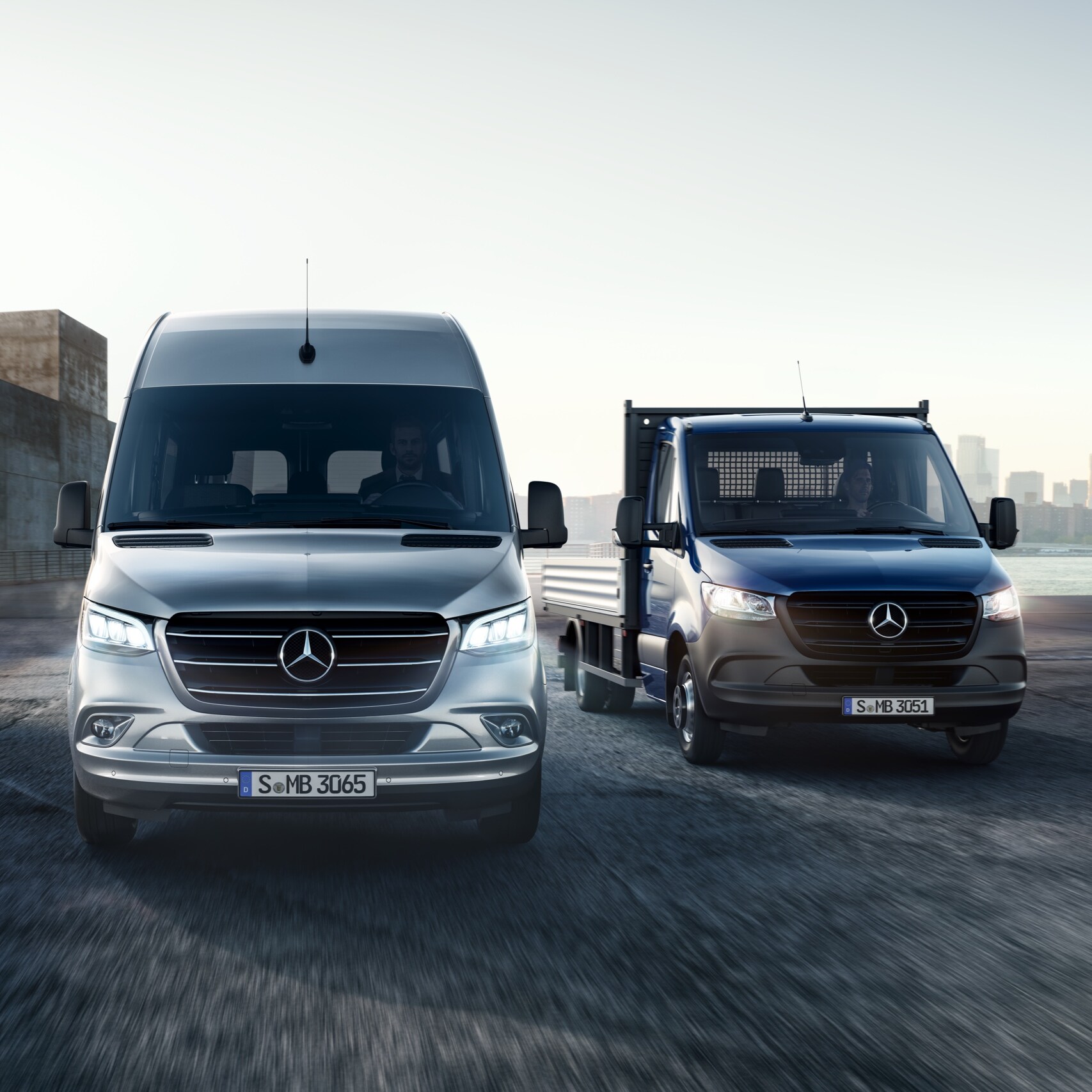 Mercedes-Benz Sprinter ในรูปแบบกระบะบรรทุกและรถตู้บรรทุกแบบทึบ จอดข้างกันที่หน้ากลุ่มอาคารสมัยใหม่